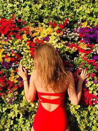 Rear view of woman wearing red swimsuit standing against flowering plants