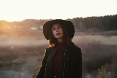 Portrait of young woman looking away against sky during sunset