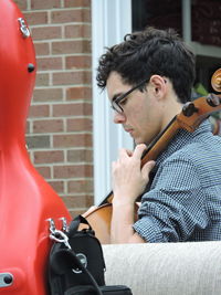 Side view of man playing cello against building