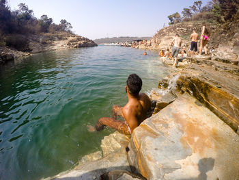 Full length of shirtless man on rock in sea