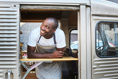 Smiling mid adult male owner looking away while standing in food truck