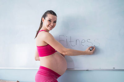 Portrait of smiling young woman standing against wall