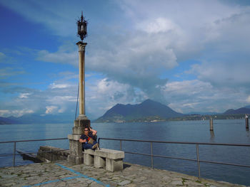 Lighthouse on sea by mountain against sky