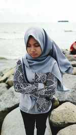 Sad young woman wearing hijab standing at beach