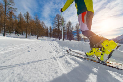 Low section of person skiing on snow against sky