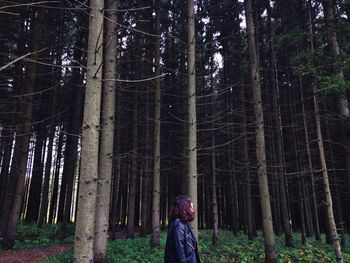 Woman standing by tree trunk in forest