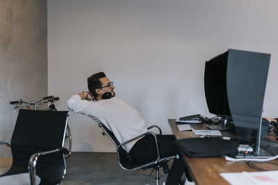 Young businessman with hands behind head while working on computer in creative office