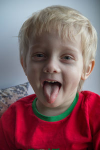 A little blonde boy in a red t-shirt smiles and shows his tongue. he's fun. close-up portrait.