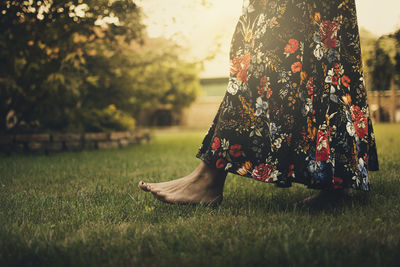 Low section of woman wearing floral patterned dress while walking on grass