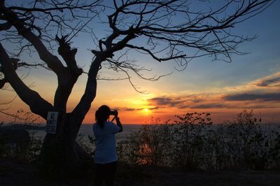 Silhouette woman standing by tree against sky during sunset