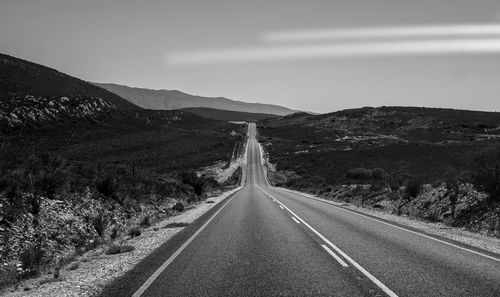 Empty road leading towards mountain against sky