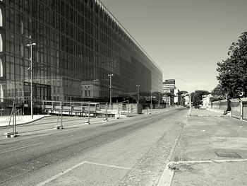 Empty road by buildings against sky in city