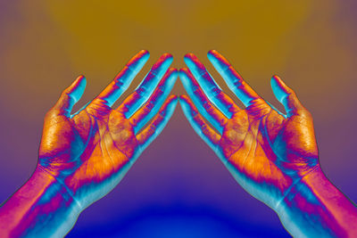 Close-up of hands over illuminated colored background