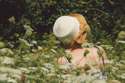 Rear view of woman wearing hat while sitting in flowering field