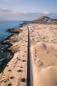 Road amidst sand by sea