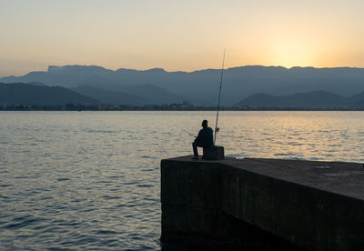 Silhouette man fishing on sea against sky during sunset