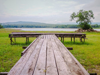 Empty bench on field against sky