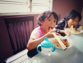 Portrait of siblings having lunch using chopsticks at home