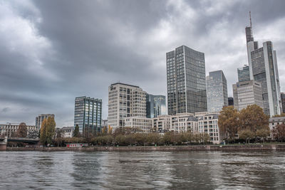 Buildings by river against cloudy sky