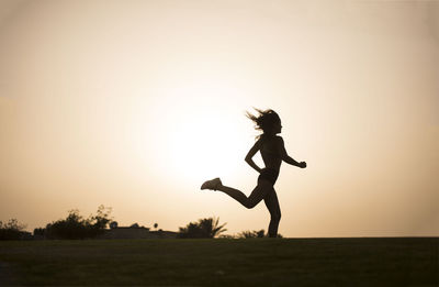 Silhouette woman running on field against sky during sunset