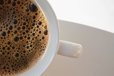 Close-up of white cup with fresh hot black coffee with bubbles on the surface