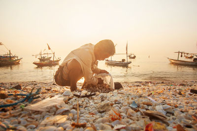 Rear view of man sitting on beach against clear sky