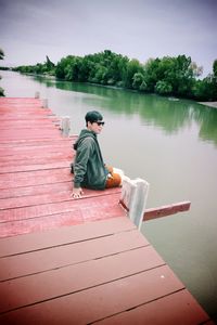 Man sitting on pier over lake against sky