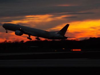 Silhouette of airplane flying in sky at sunset