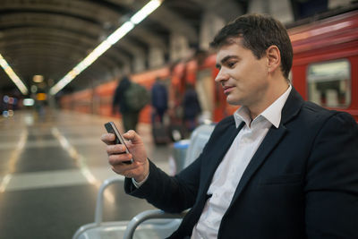 Businessman using mobile phone while sitting at subway station