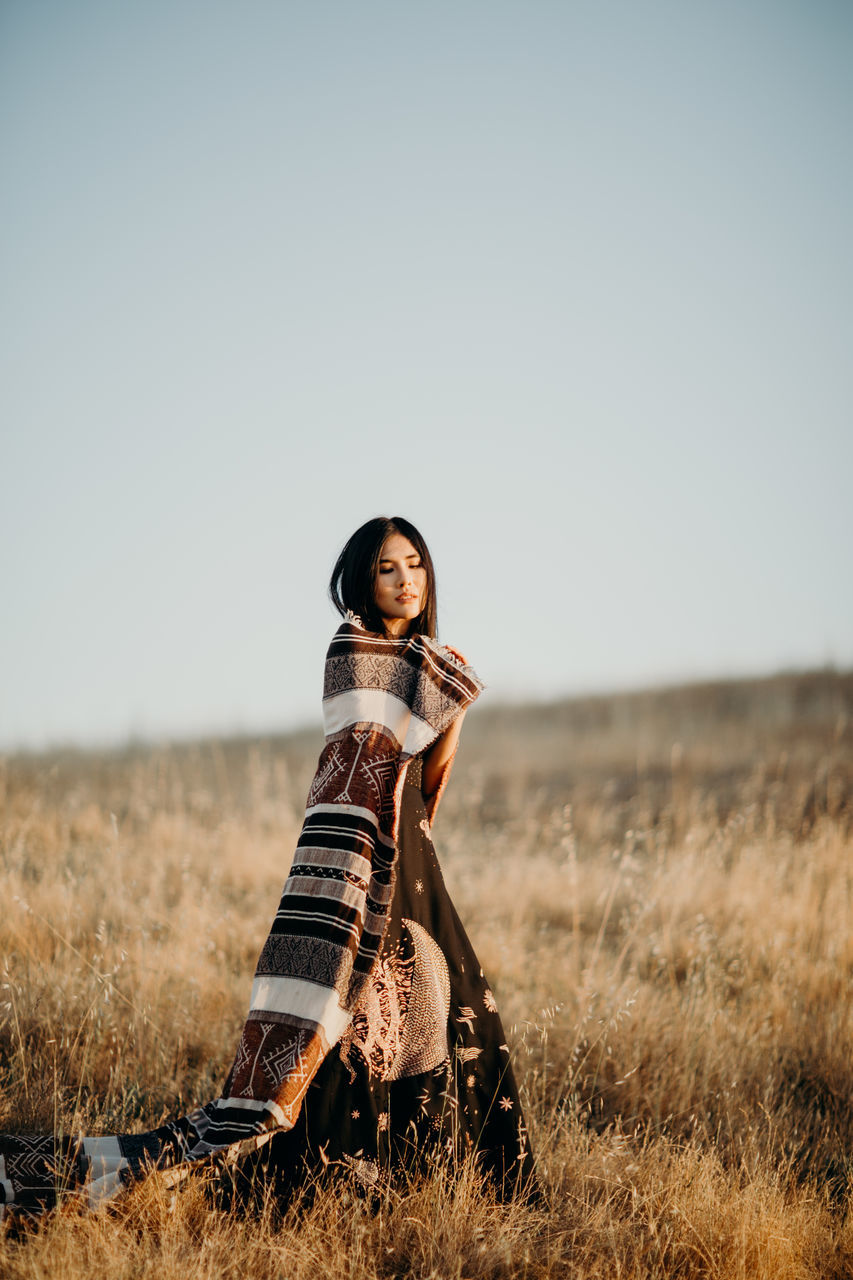 sky, land, one person, field, clear sky, nature, grass, portrait, plant, full length, leisure activity, standing, copy space, young adult, looking at camera, real people, women, day, casual clothing, outdoors, beautiful woman