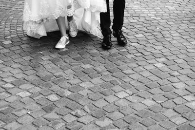 Low section of bride and groom walking on cobblestone