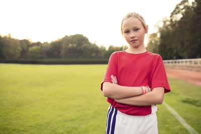 Portrait of confident female soccer player standing with arms crossed on field