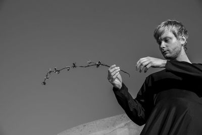 Low angle view of man holding plant against sky