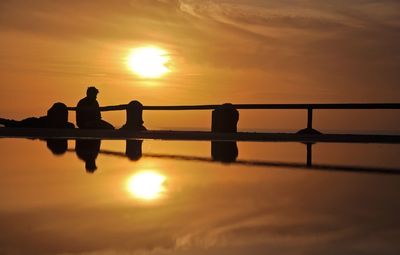 Silhouette people standing by sea against sky during sunset