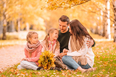 Full length of father and girl sitting on autumn leaves