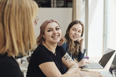 Smiling female entrepreneurs looking at colleague during meeting in office