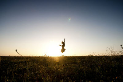 Woman jumping over field against sky during sunset