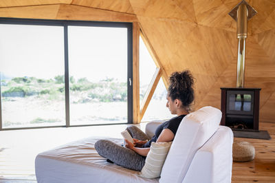 Woman using e reader while relaxing in a wooden dome tent.