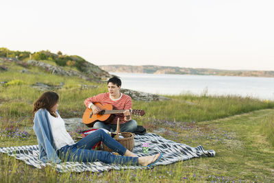 Man playing guitar for girlfriend while enjoying picnic