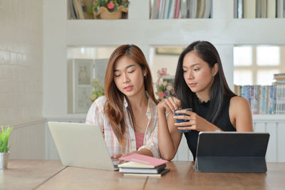 Young woman using phone while sitting on table