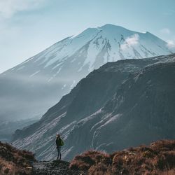 Rear view of person standing on snowcapped mountain against sky