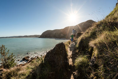 Father and young son walking on mountain path above ocean in new zealand