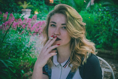 Portrait of young woman smoking cigarette against plants