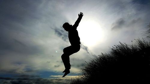 Low angle view of silhouette man jumping against sky