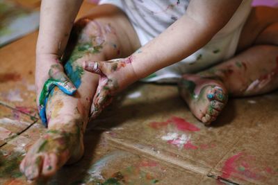 Low section of playful child with hands and legs painted sitting on floor