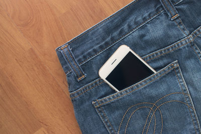 High angle view of mobile phone in back pocket of jeans over table