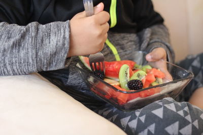 Midsection of boy eating fruits while sitting on sofa at home