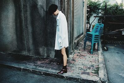 Side view of young woman standing against building