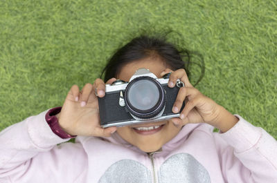 Portrait of smiling girl photographing with camera on grassy field
