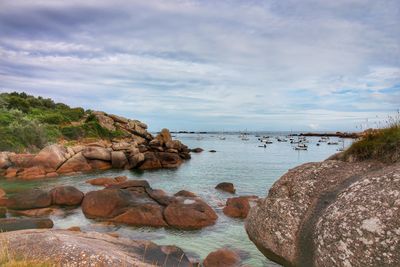 Rock formations at sea against cloudy sky